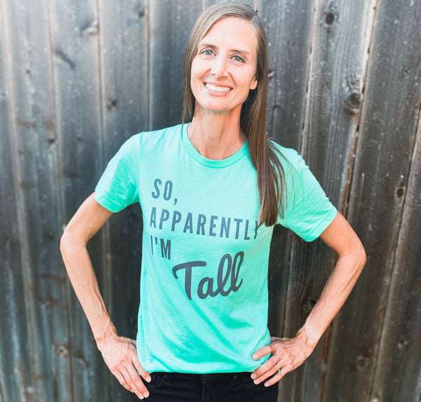 A tall woman modeling a funny, graphic t-shirt that says "So, Apparently I'm Tall".