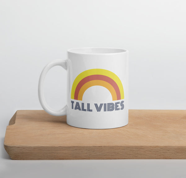 White, ceramic 11 oz coffee mug with a rainbow and the phrase "Tall Vibes"